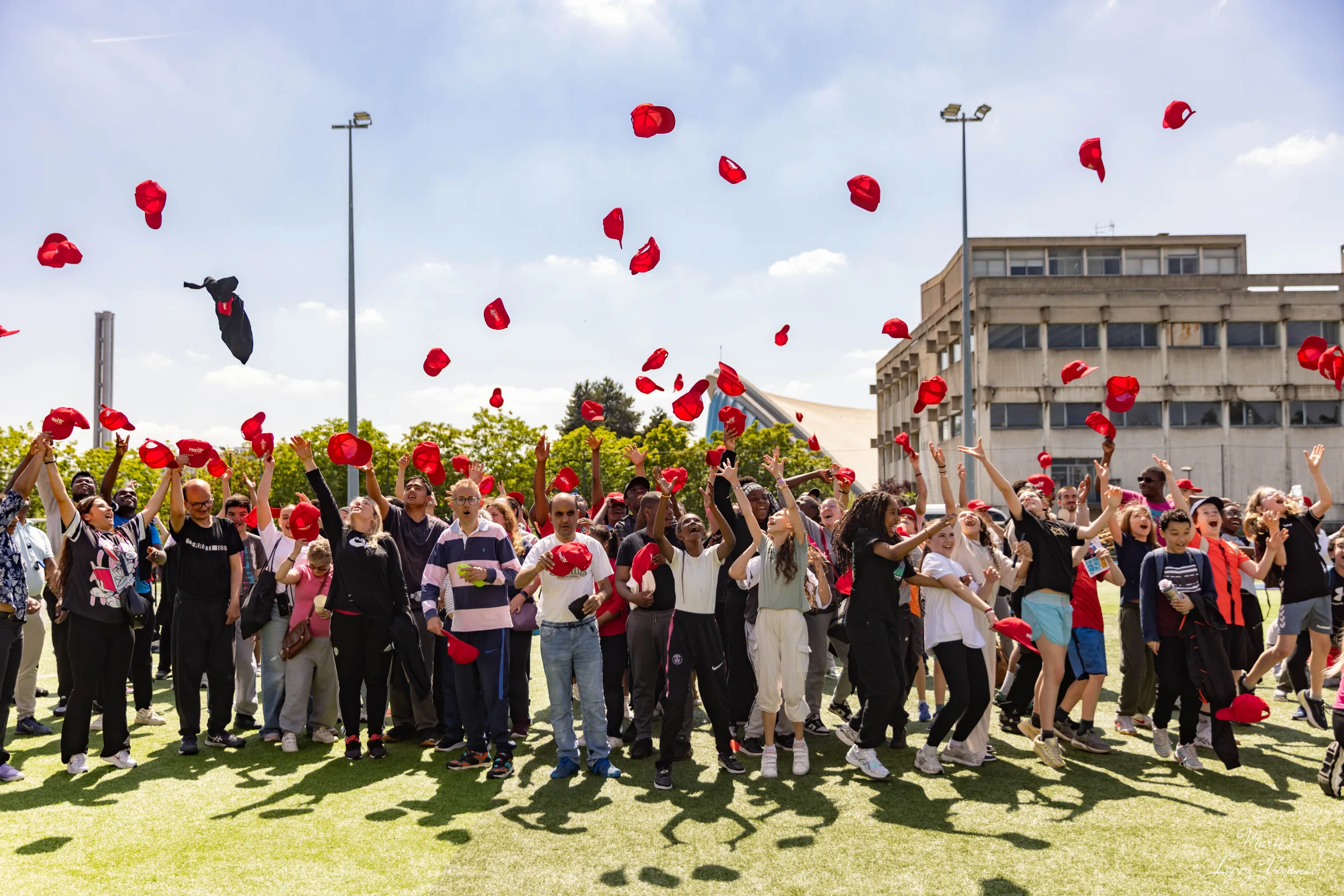 Des participantes et participants lancent des casquettes rouges lors d’un rassemblement sportif en extérieur.