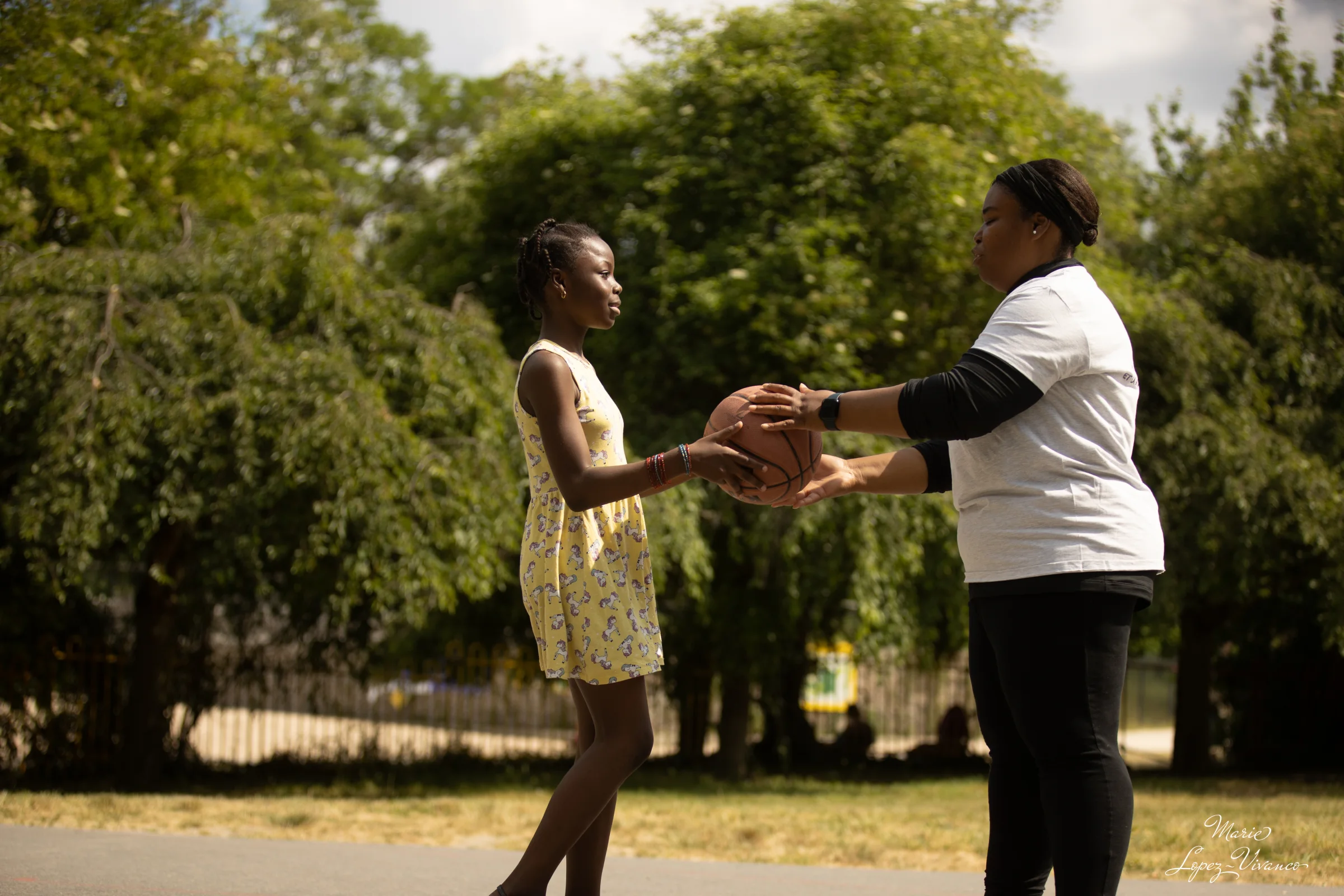 Une adulte et une enfant se passent un ballon de basket dans un parc.